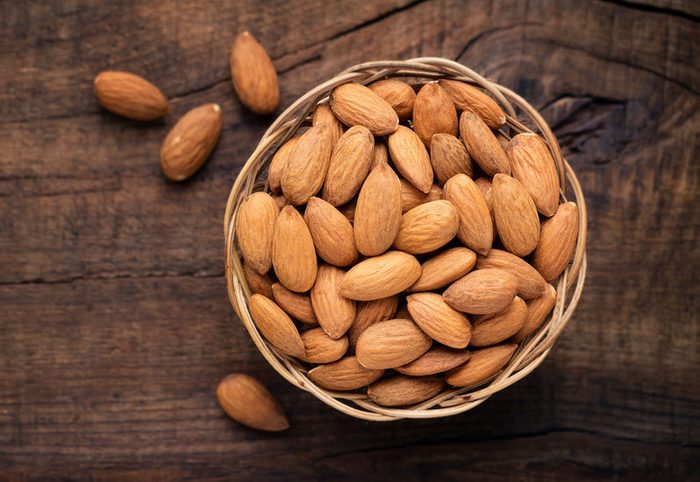 Almonds in willow bowl against dark rustic wooden background. Overhead view