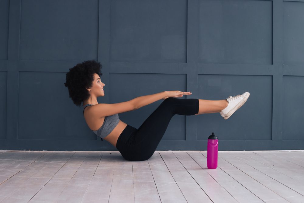 Take care of your body and it will take care of you! Beautiful African American young woman doing abdominal crunches indoors.