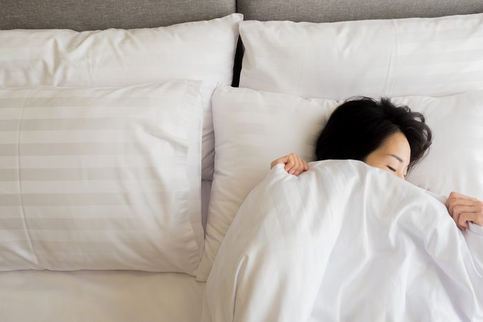 Sleeping woman cover face with blanket flat lay. Close-up of young women, sleeping under white blanket and covering half face.