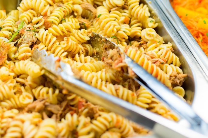 Buffet tray of pasta with utensils in it.