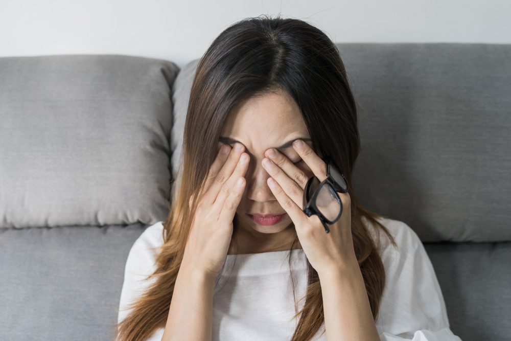 woman holds her glasses and rubs her eyes 