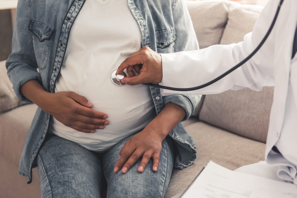 Handsome Afro American doctor in white coat is consulting beautiful pregnant woman in his office