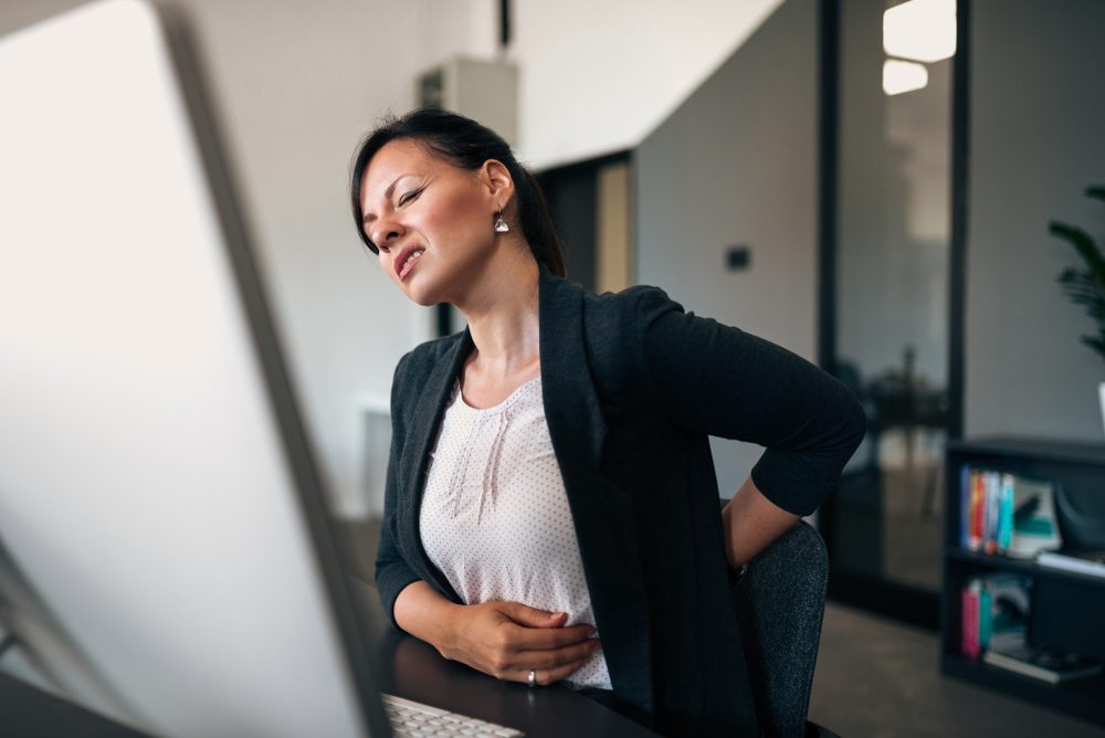 Beautiful young businesswoman having back pain while sitting at office desk.