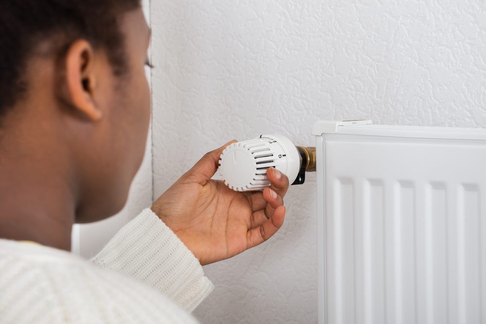 Woman Adjusting Temperature Of Radiator Using Thermostat