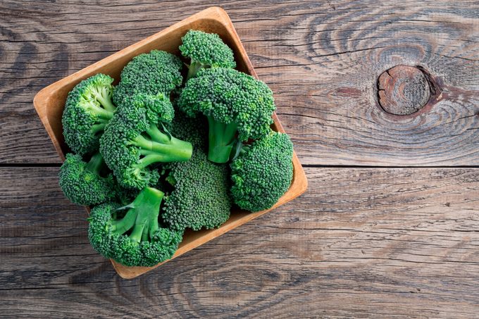 fresh raw green broccoli in wooden bowl on wooden background, top view