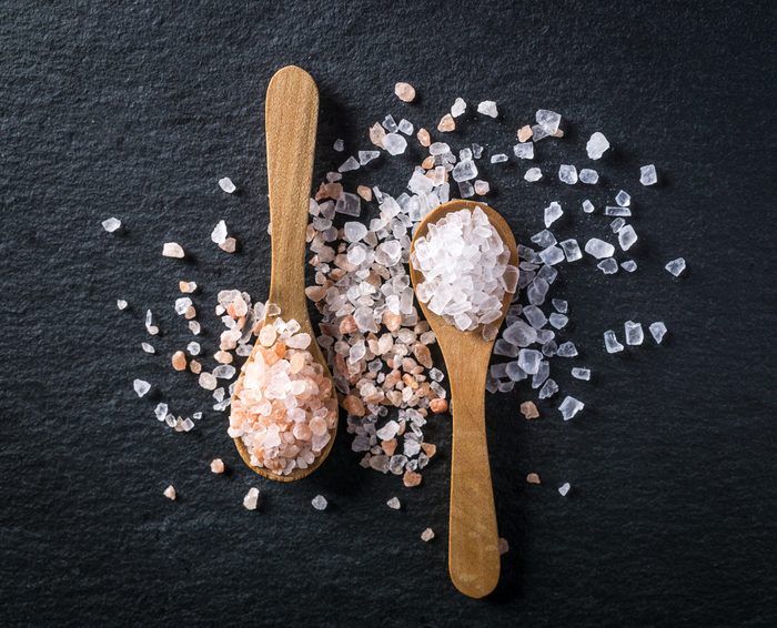 Two wooden spoons with pink himalayan and white kithchen salt on dark stone background. Salt collection, top view