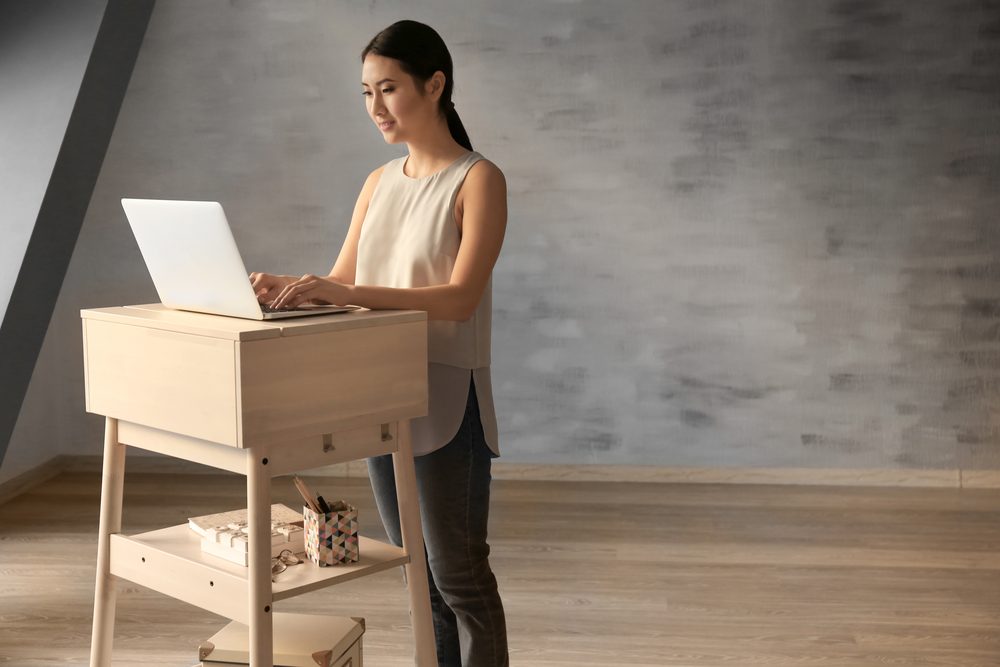 Asian woman typing on laptop at stand-up workplace