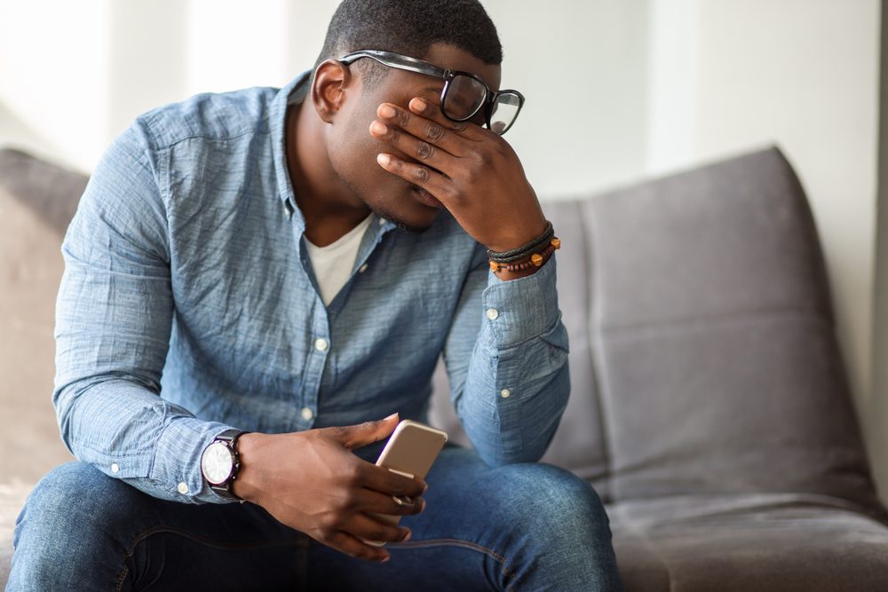 Feeling exhausted. Frustrated young black man massaging his nose and keeping eyes closed while sitting at his working place in office