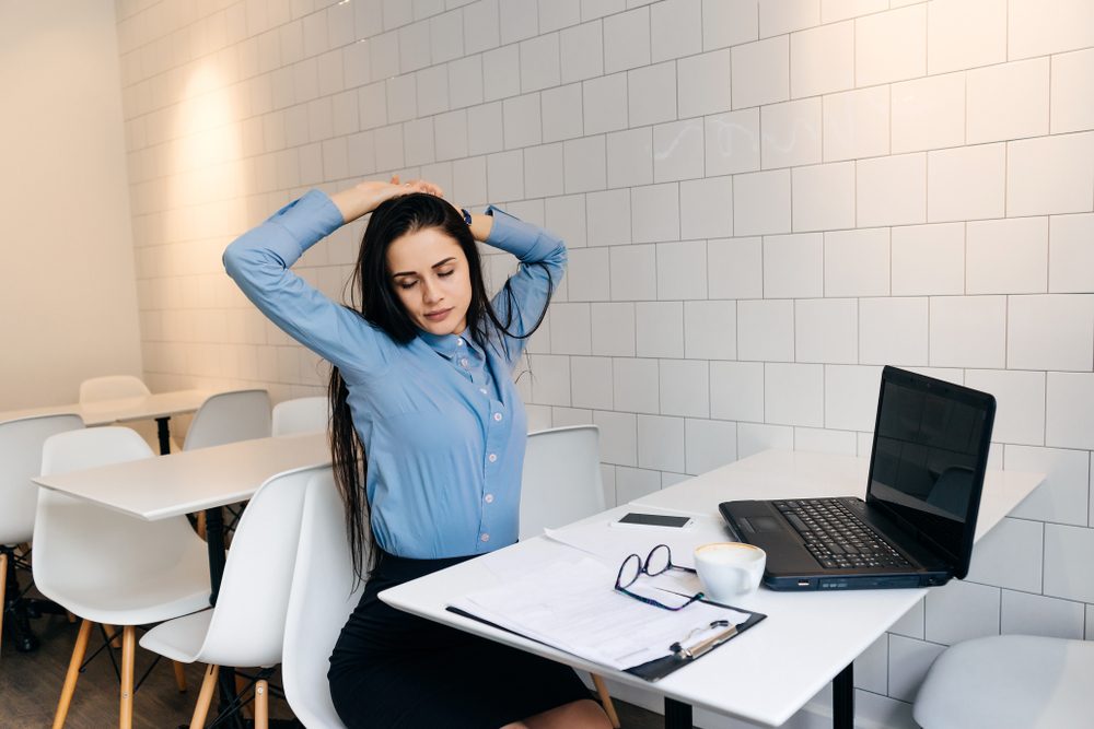 young brunette girl in a blue shirt is sitting in a cafe after work