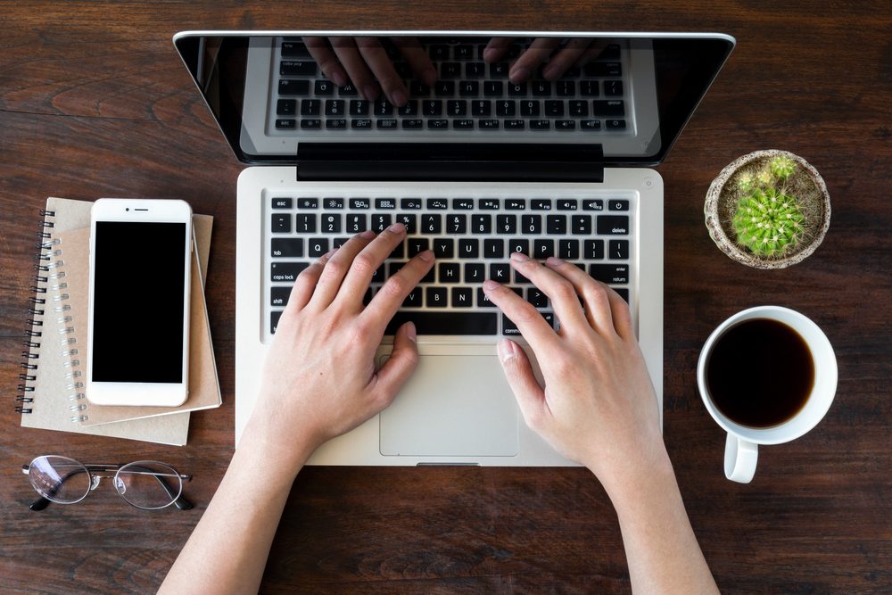 A man is working by using a laptop computer on vintage wooden table. Hands typing on a keyboard. Top view.