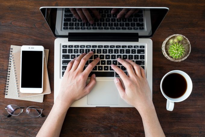 A man is working by using a laptop computer on vintage wooden table. Hands typing on a keyboard. Top view.