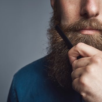 close up of young man brushing his beard