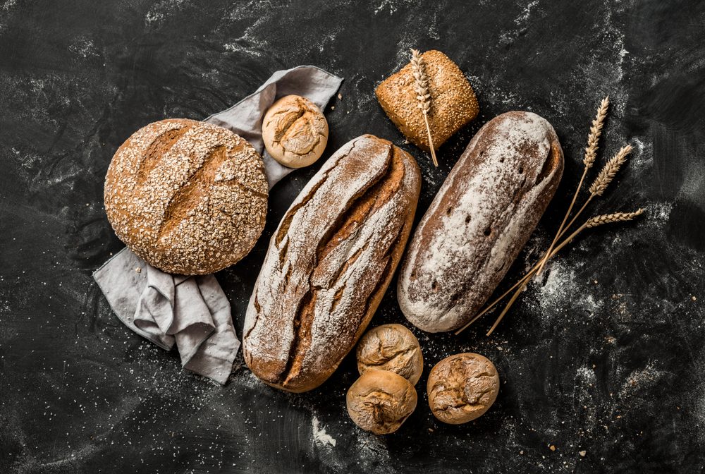 Bakery - gold rustic crusty loaves of bread and buns on black chalkboard background. Still life captured from above (top view, flat lay).