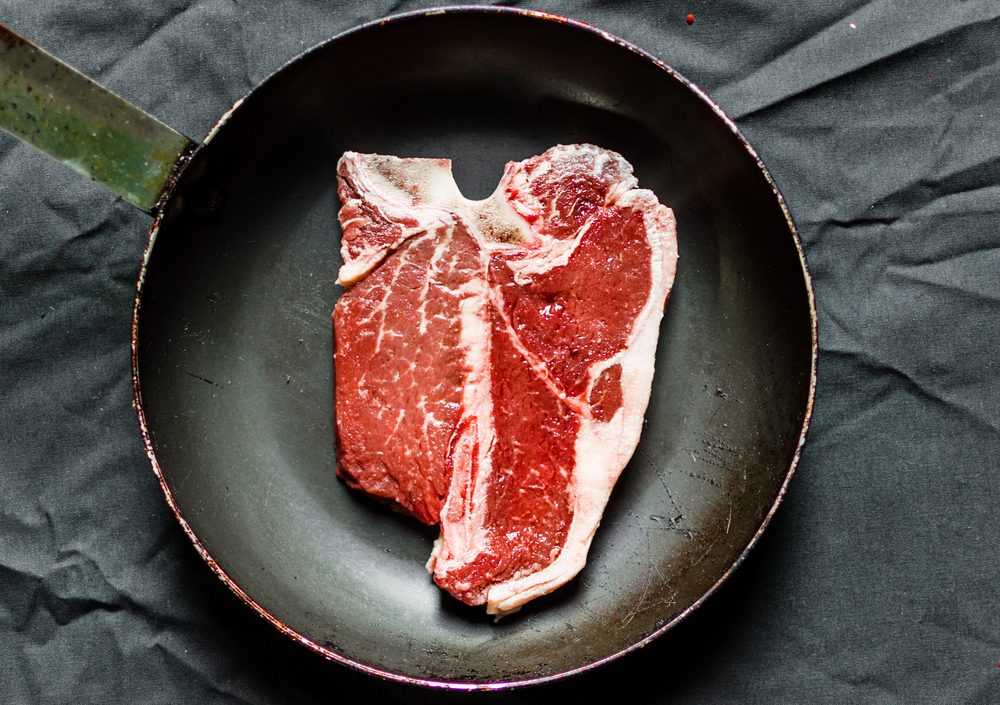 Raw T bone steak of beef meat in a frying pan against black background. Selective focus.