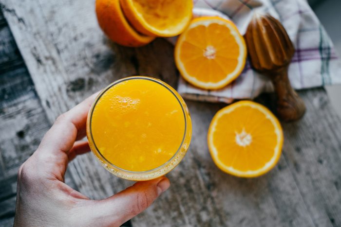 Woman Hand with juice glass and Oranges on wooden background.