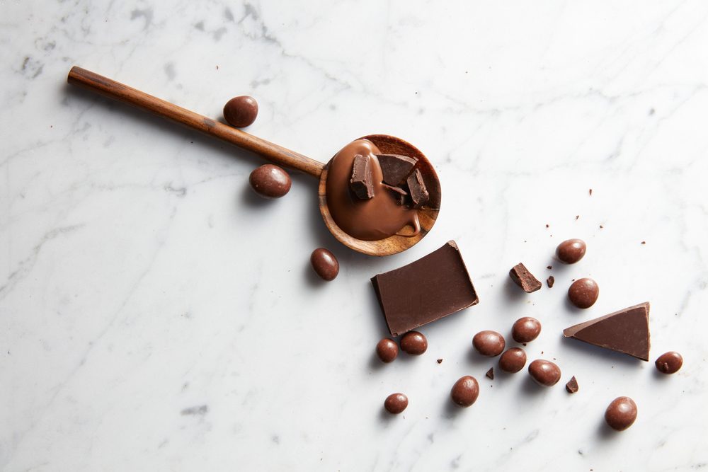 wooden spoon with caramel, chocolate chips and chocolate balls on white marble background