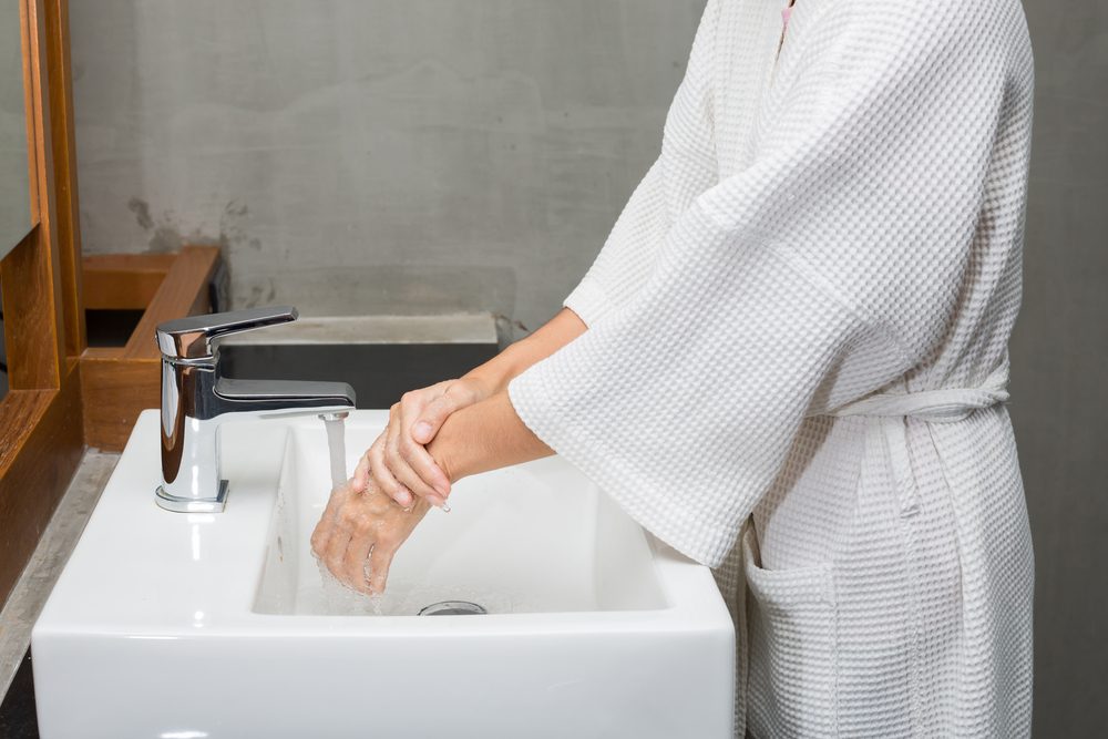 Woman in a bathrobe is washing hands.