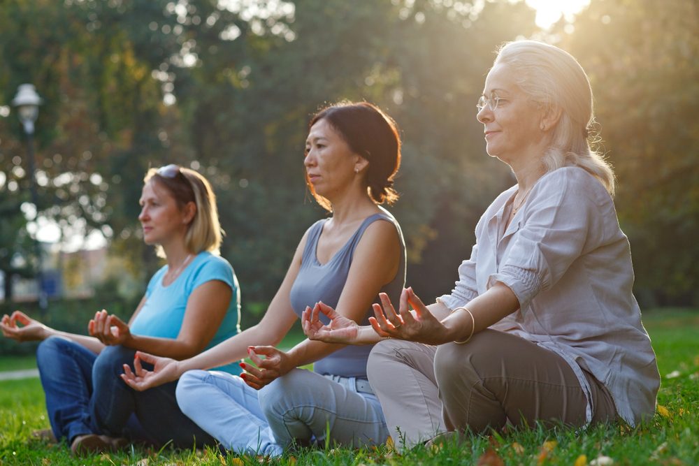 Three ladies meditate while sitting on the grass