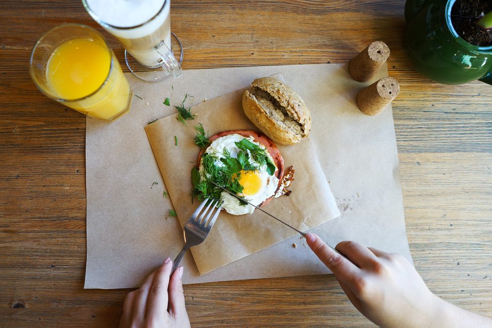 Hands of the girl cut the eggs on paper, served with bread, herbs, sausage and fresh juice.