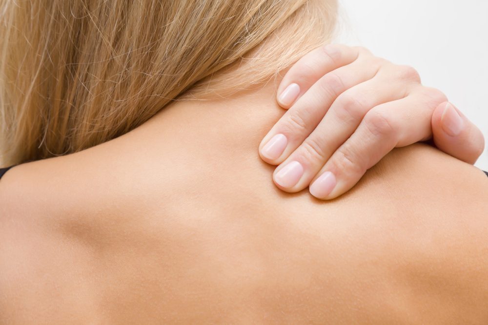 Young, blonde woman massaging her naked shoulder with hand. Pain from strain and incorrect posture. Inactive lifestyle.