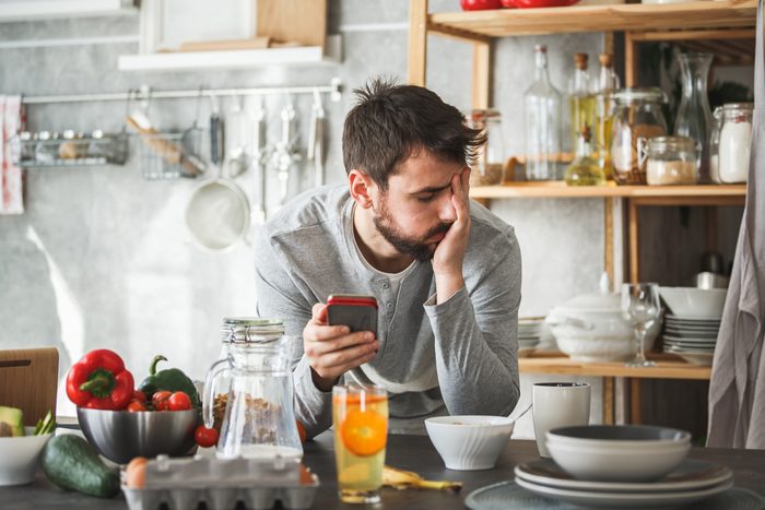 upset man at home in kitchen with his phone