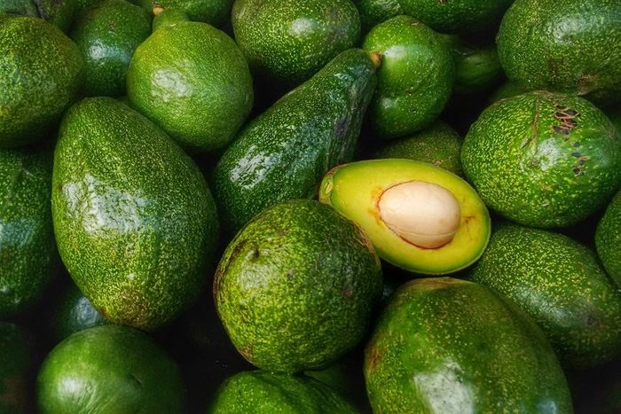 Bunch of green Avocados. One of them is opened that the stone and the pulp are visible.