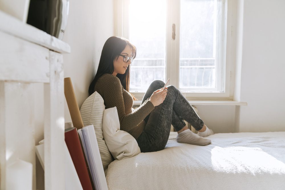 woman using phone while sitting on bed
