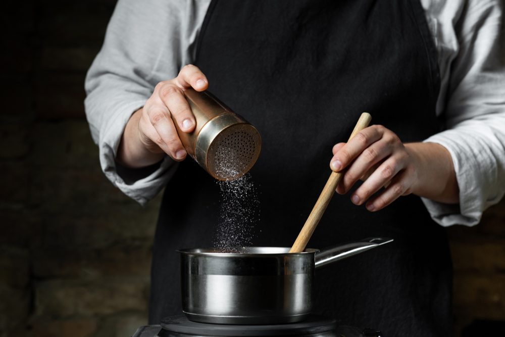 Cooking food in metal saucepan, adding salt by chef hands. Food concept background.
