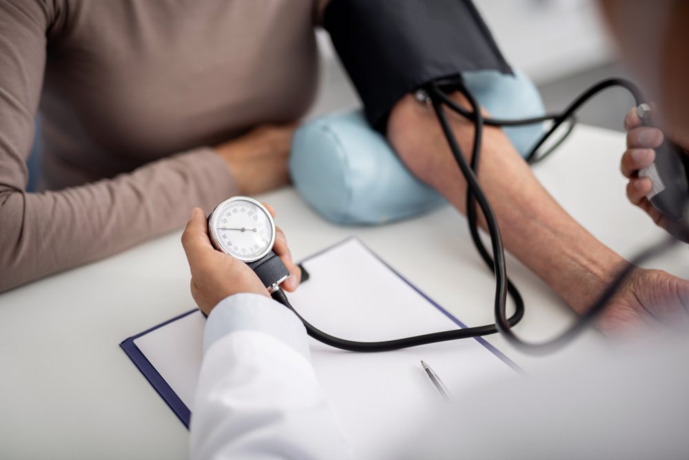 Careful experienced practitioner sitting with his patient and holding a gauge while measuring blood pressure