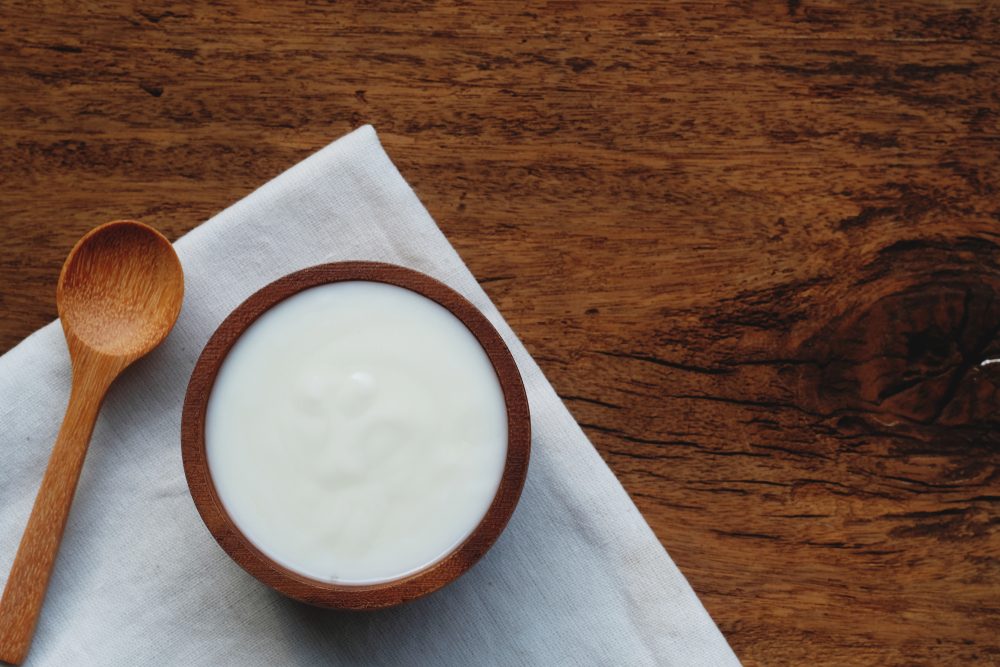 Plain organic yogurt in wooden bowl and wood spoon on wood texture background, copy space