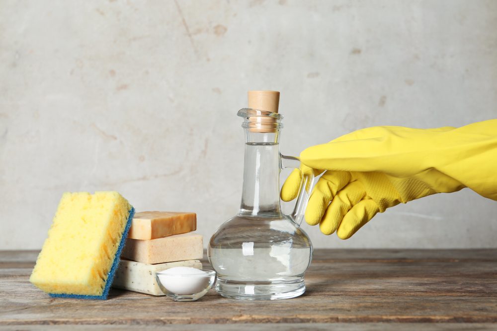 Woman with jug of vinegar and cleaning supplies at table