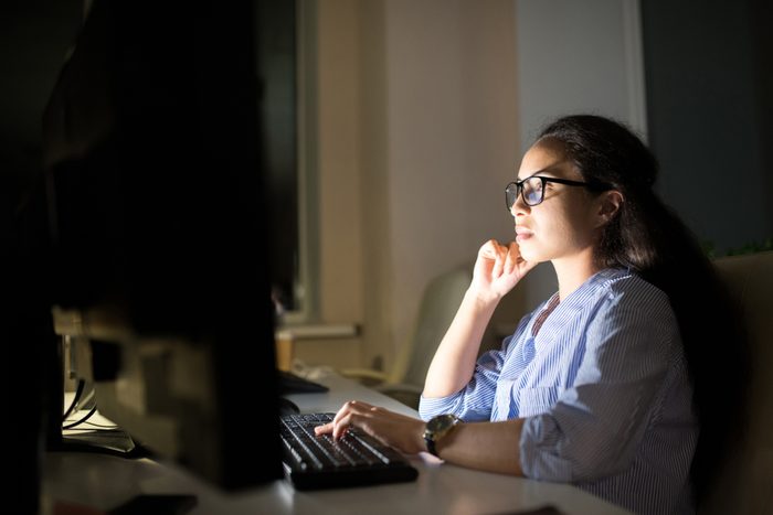 Side view portrait businesswoman working at computer late at night in dark office, copy space