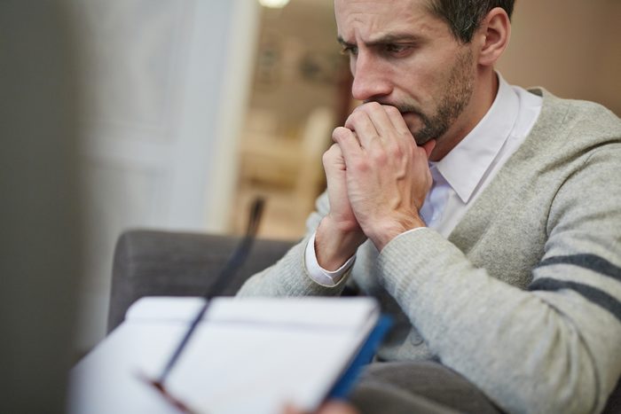 Waist-up portrait of disappointed bearded patient absorbed in thoughts while his psychiatrist filling in medical card