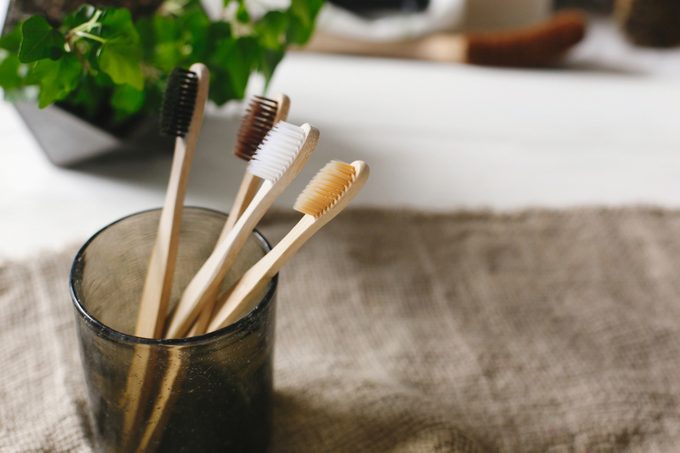 eco natural bamboo toothbrushes in glass on rustic background with greenery. sustainable lifestyle concept. zero waste home. bathroom essentials, plastic free items