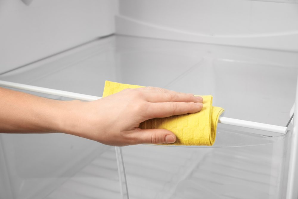 Woman cleaning refrigerator with rag, closeup
