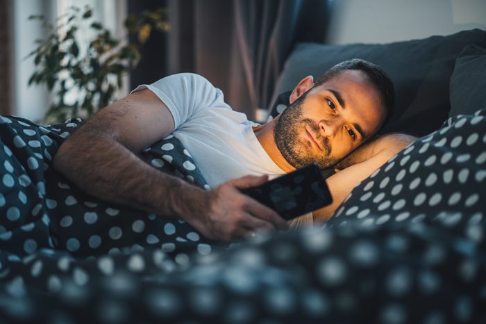 young cell phone addict man awake at night in bed using smartphone for chatting, flirting and sending text message in internet addiction and mobile abuse concept