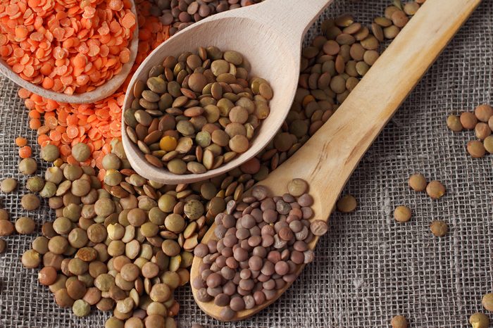 Green and red lentils in wooden spoons on sackcloth