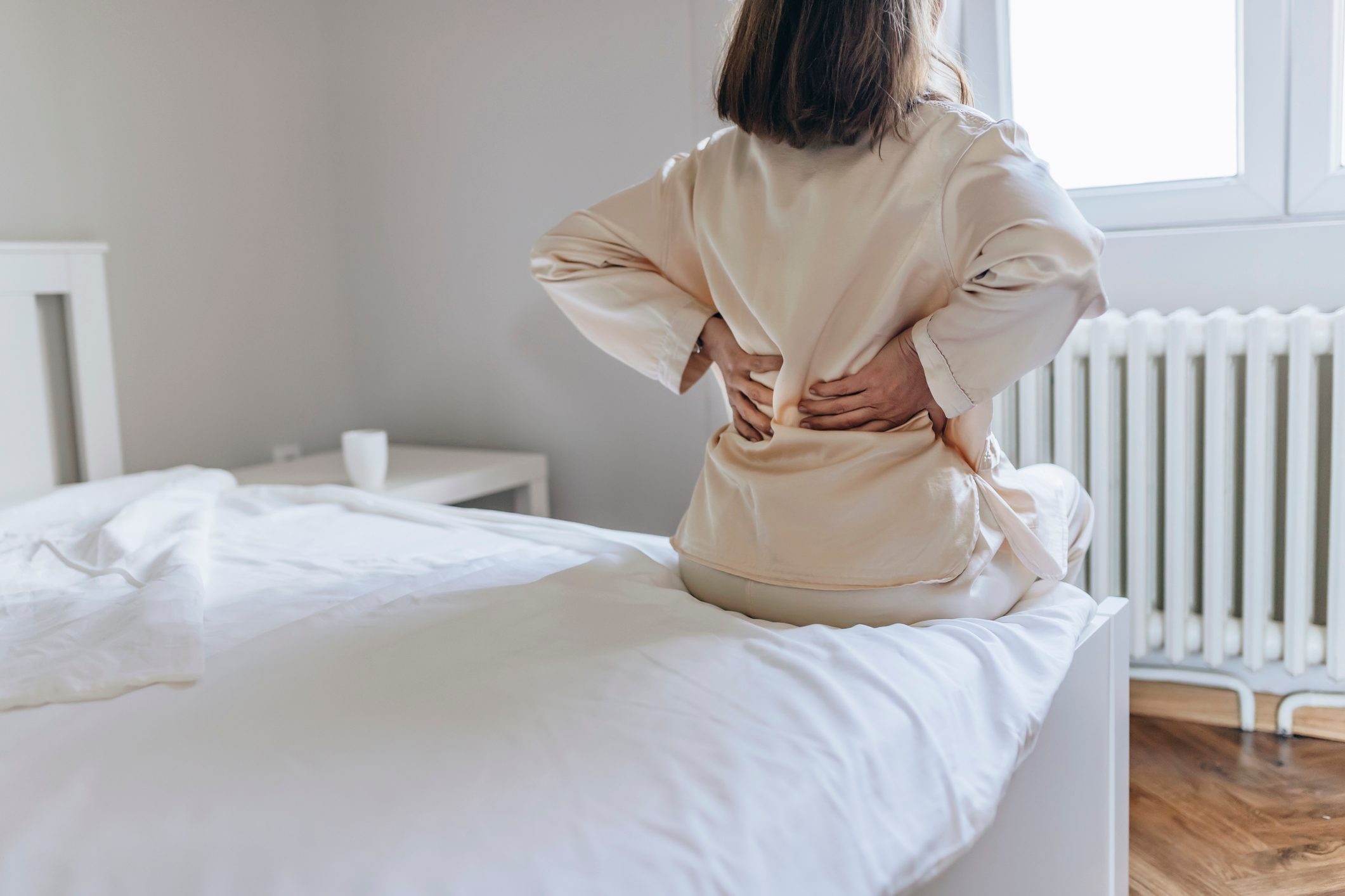 woman sitting on edge of bed with hands holding back