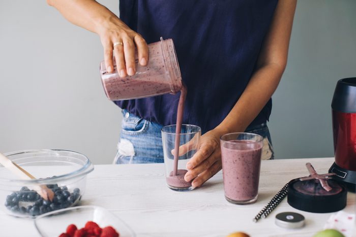 woman pouring fresh fruit smoothie into glass