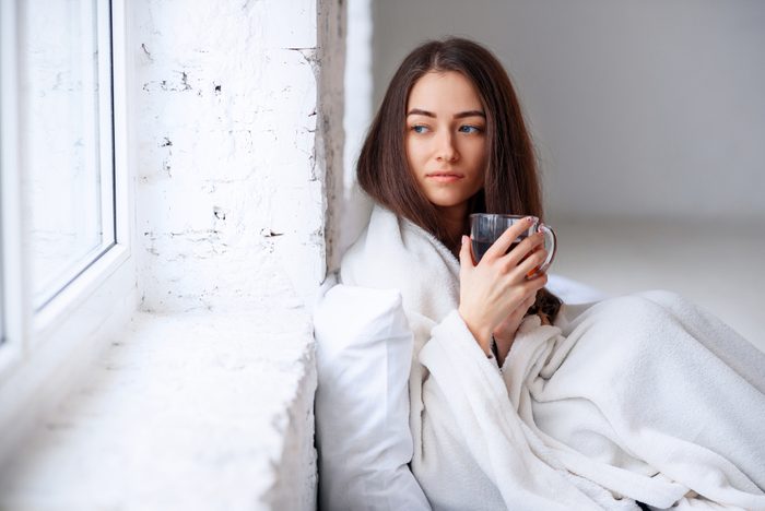 Close up of beautiful young woman in warm plaid with hot cup of tea in hands. Sickness and illness. Sick unhealthy female drinking warm drink indoors.