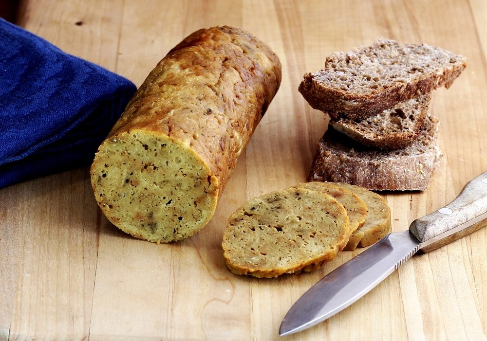 A healthy vegan snack: A roll of vegan seitan on a cutting board with slices of rye bread