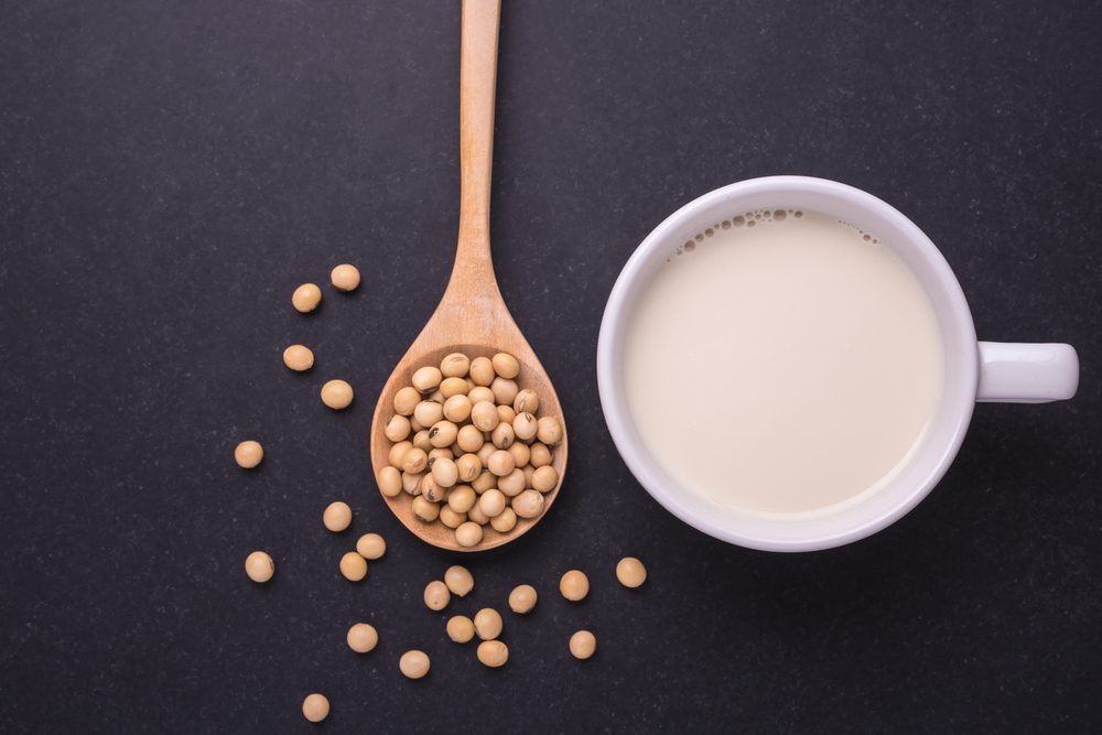 Soy milk in white cup and soy bean on dark table background. Top view