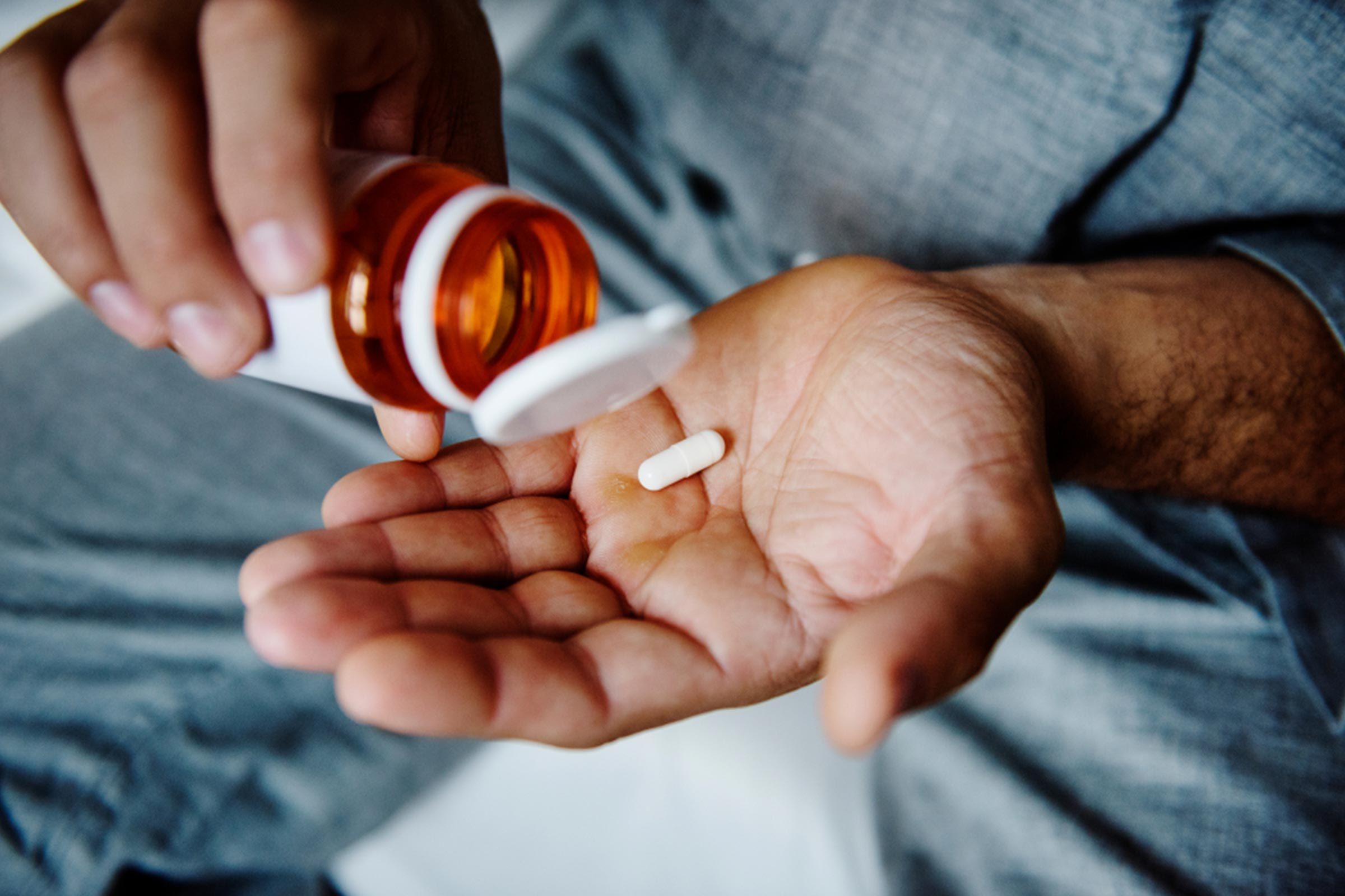 Someone shaking prescription medication out of a bottle into his hand.