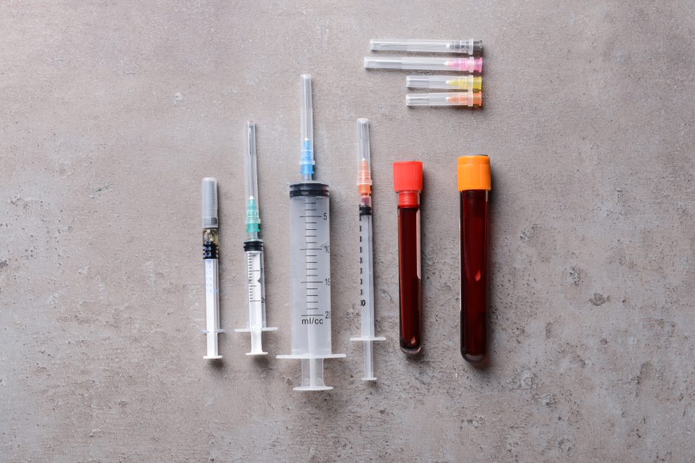 Syringes and test-tubes with blood on grey background. Health care concept