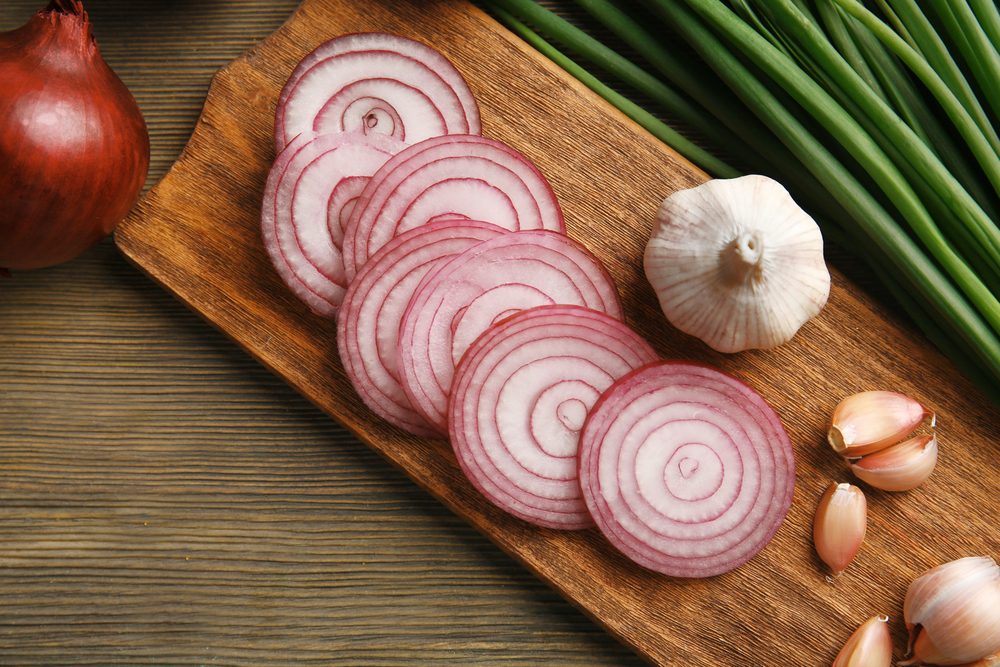 Red onions circles, green onion with garlic on board against wooden background