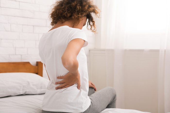 African-american woman having back pain after sleep, sitting on bed