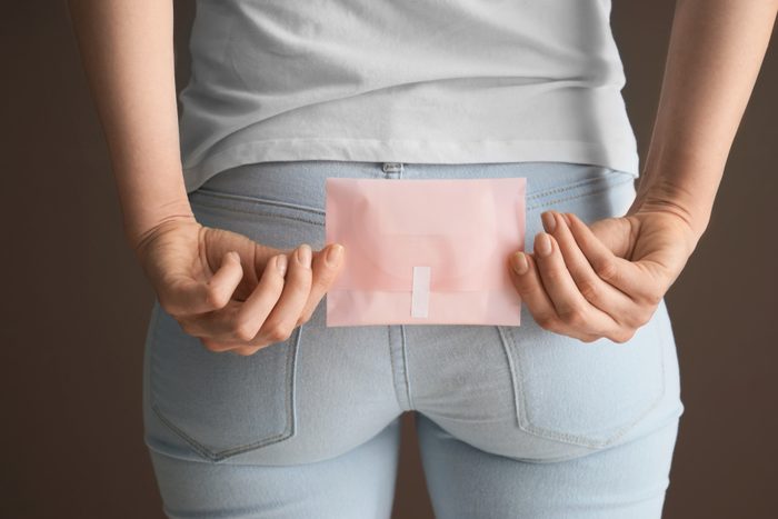 Woman holding menstrual pad behind her back on color background