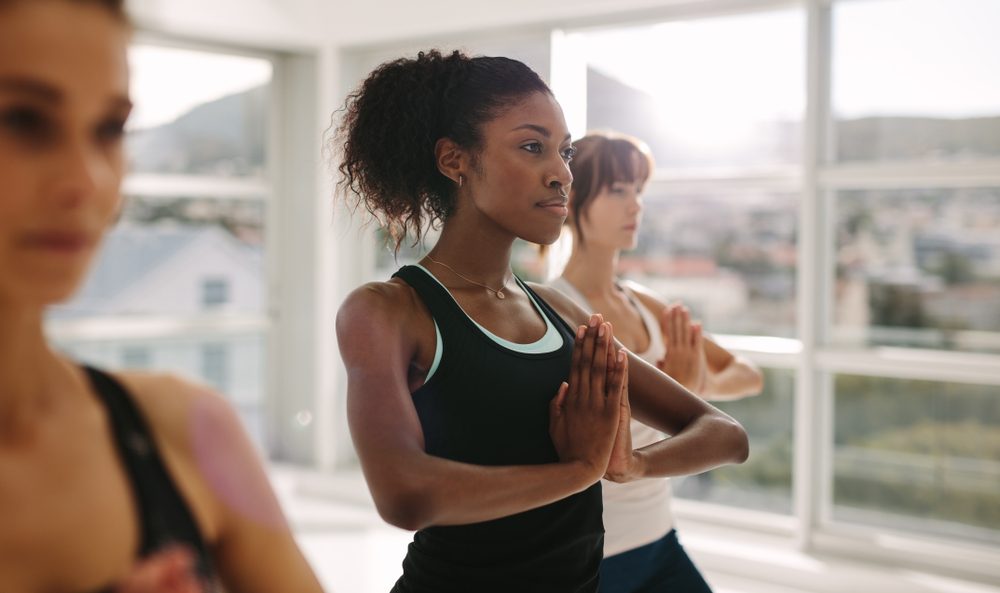 Women stretching and practices yoga in class. Healthy female doing yoga workout in fitness studio. Standing with hands joined.