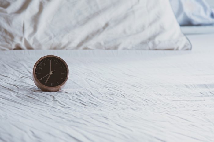 A analog alarm clock on wrinkled bed sheets white color in the morning