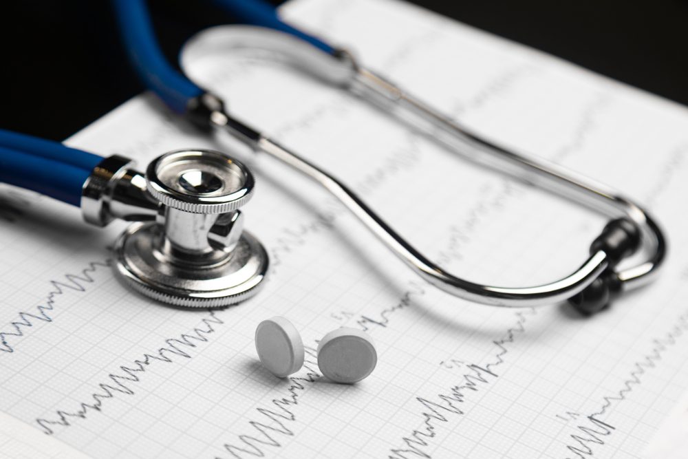 Stethoscope and two tablets on edge lie on a sheet with an electrocardiogram